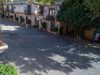 a cobblestone road lined with trees and buildings in an apartment complex courtyard area