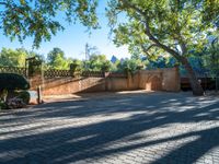 a brick walkway that has trees and a stone wall with some bushes on it and another fence