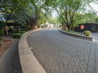 a brick sidewalk next to a gate and some trees and bushes in a residential area