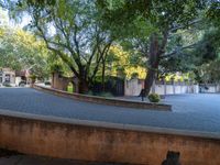 a long curved wall is between two trees and plants on a brick road in a residential area