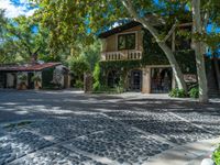 a house surrounded by lots of leaves and trees next to a driveway area with cobblestone sidewalk