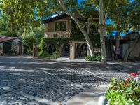 a house surrounded by lots of leaves and trees next to a driveway area with cobblestone sidewalk