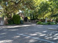 a driveway in the middle of a courtyard with trees and landscaping surrounding it and an archway