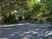 a driveway in the middle of a courtyard with trees and landscaping surrounding it and an archway