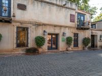 an old stone building is next to an entrance and patio with potted plants and bushes