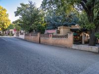 a lone street that is lined with trees, houses, and benches next to a fence