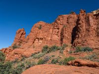 a red rock formation, with trees, bushes and rock formations on the far side