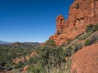 a hillside with tall red rocks in the desert by a mountain range near trees and bushes