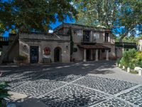 a very nice building with stone floors on a patio and a tree in front of it