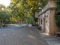 a sidewalk that runs between buildings and trees near a fountain in the courtyard of an historic residence