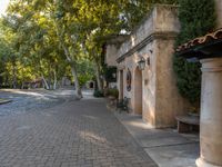 a sidewalk that runs between buildings and trees near a fountain in the courtyard of an historic residence