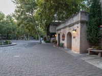 a sidewalk that runs between buildings and trees near a fountain in the courtyard of an historic residence