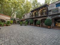 a building with a stone courtyard and trees and bushes inside it and the building has plants growing on top of the roof