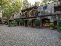 a building with a stone courtyard and trees and bushes inside it and the building has plants growing on top of the roof