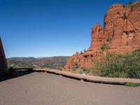 a person riding on a bike near some red rock formations and trees and a lake