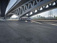 a semi truck is under a large bridge in the sun while some other vehicles are waiting under