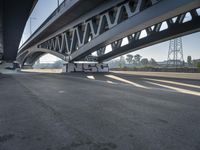 a semi truck is under a large bridge in the sun while some other vehicles are waiting under