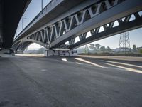 a semi truck is under a large bridge in the sun while some other vehicles are waiting under