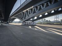 a semi truck is under a large bridge in the sun while some other vehicles are waiting under