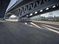 a semi truck is under a large bridge in the sun while some other vehicles are waiting under