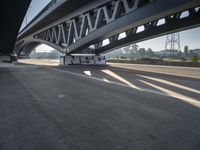 a semi truck is under a large bridge in the sun while some other vehicles are waiting under