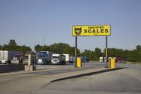 a large group of semi trucks lined up behind a large sign for a scale shop