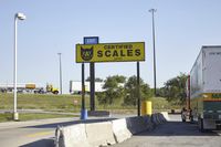 a large group of semi trucks lined up behind a large sign for a scale shop