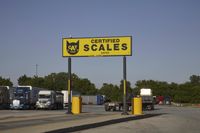 a large group of semi trucks lined up behind a large sign for a scale shop