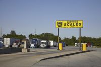 a large group of semi trucks lined up behind a large sign for a scale shop
