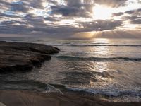 there is a surfboard on the rocks on the beach at sunset, and you can see a person surfing the waves