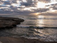 there is a surfboard on the rocks on the beach at sunset, and you can see a person surfing the waves