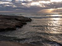 there is a surfboard on the rocks on the beach at sunset, and you can see a person surfing the waves