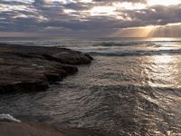 there is a surfboard on the rocks on the beach at sunset, and you can see a person surfing the waves