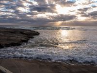 there is a surfboard on the rocks on the beach at sunset, and you can see a person surfing the waves