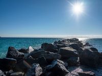 the sun is shining brightly over the calm ocean water and rocks at the shoreline of the beach