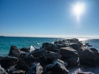 the sun is shining brightly over the calm ocean water and rocks at the shoreline of the beach