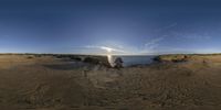 the sun is shining over the ocean on the beach rocks and sand dunes are in the foreground