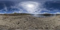 a panoramic view of rocks and a river in the foreground with a full sky with sun