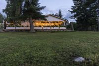 a house that is by some trees with string lights on the front of it and a lawn area