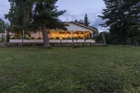 a house that is by some trees with string lights on the front of it and a lawn area