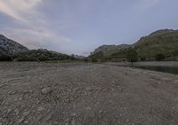 a river that is next to mountains with water and trees in it at dusk or early morning