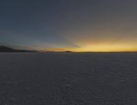 the sun rising over the vast plain behind mountains in the distance, with footprints left of the vehicle