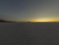 the sun rising over the vast plain behind mountains in the distance, with footprints left of the vehicle