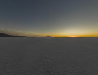 the sun rising over the vast plain behind mountains in the distance, with footprints left of the vehicle