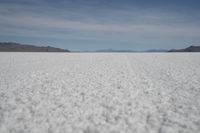 a white plain with lots of small, white rocks in the middle of it and mountains in the back