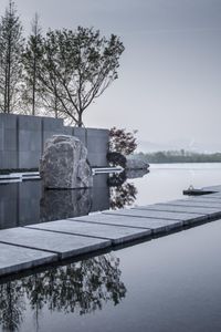 water and stepping stones next to a body of water with trees in the background and mountains reflected in the pool