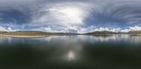 the camera is pointed out onto the water near the mountains and hills with clouds in them