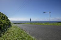 a street with no one riding on it near the ocean and grass and bushes on either side