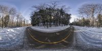 a snow - covered road that has a yellow line in the middle of it near trees