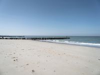 a beach with a pier over the water next to a sandy shore line and waves